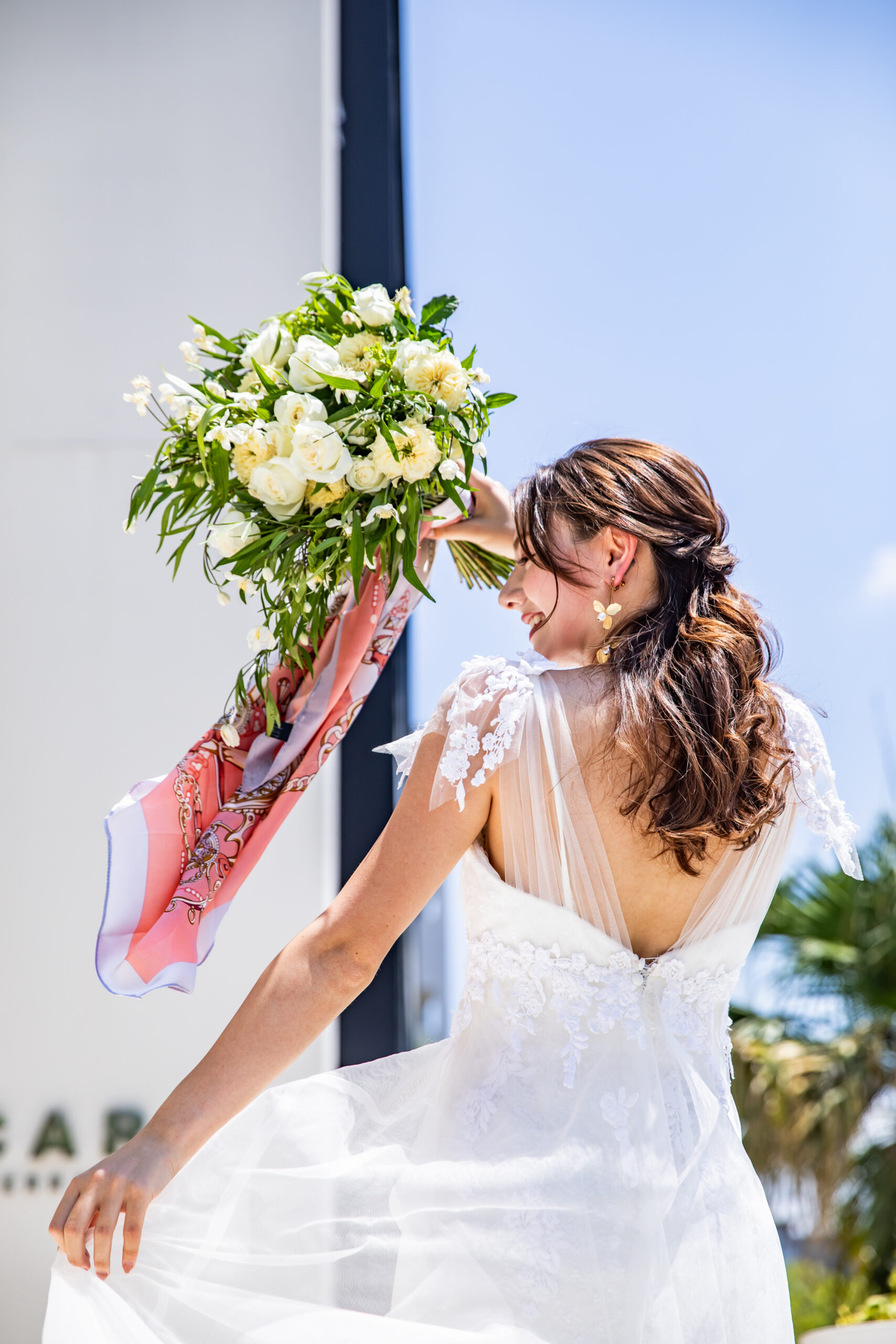 【名古屋市結婚式場ビアンカーラテラス】の開放的な空間にて、青空を背に笑顔で振り返る美しいドレス姿の花嫁様。名古屋市にある市の中心部で叶える、光と風を感じる屋上テラスでのロケーションフォトは、名古屋市内でも開放感あふれる結婚式を求めるお二人の幸せな瞬間を詳細に描写しています。