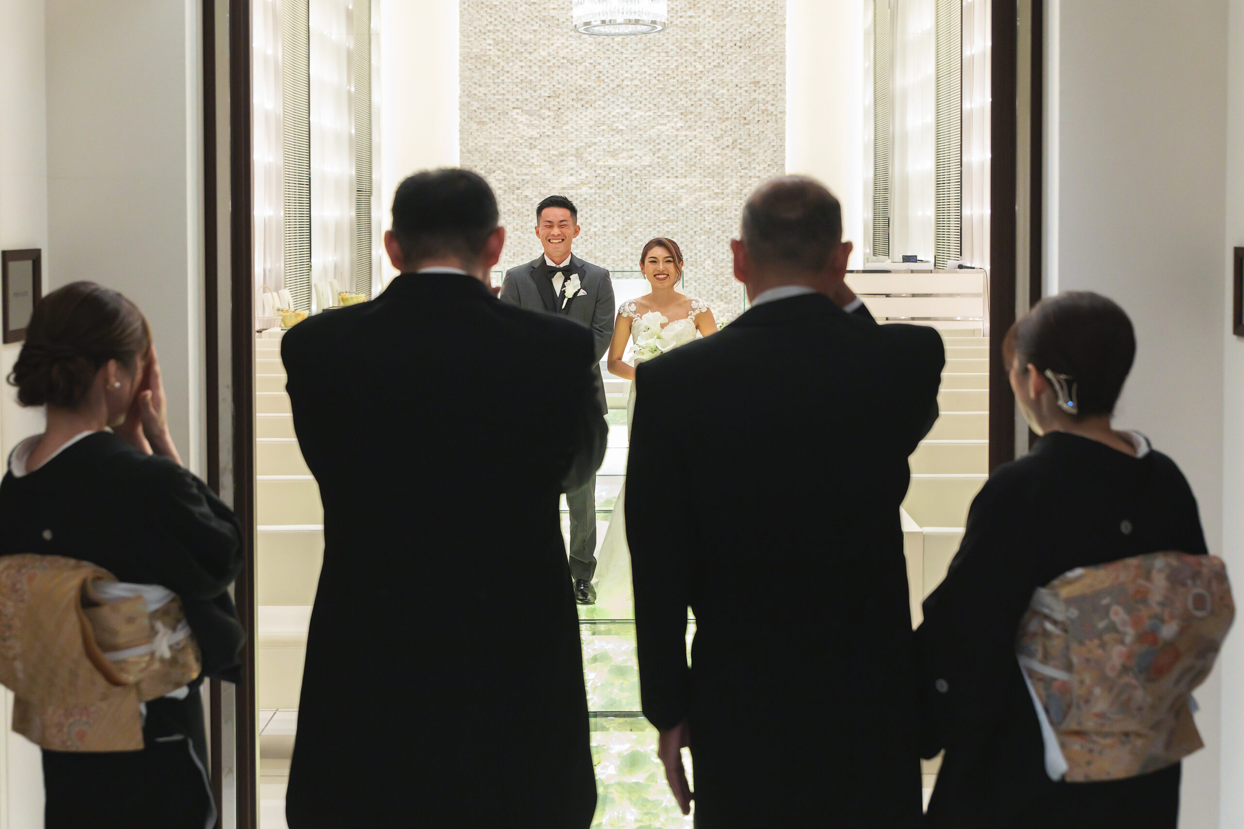 【名古屋市結婚式場ビアンカーラテラス】挙式を前に、正装したご両親へ晴れ姿を披露する感動的なペアレンツミートの瞬間。名古屋市にある市の中心部で過ごすこのかけがえのない時間は、名古屋市内で式を挙げる多くの新郎新婦様が大切にされる親孝行の場面であり、絆を再確認する美しい情景を詳細に描写しています。