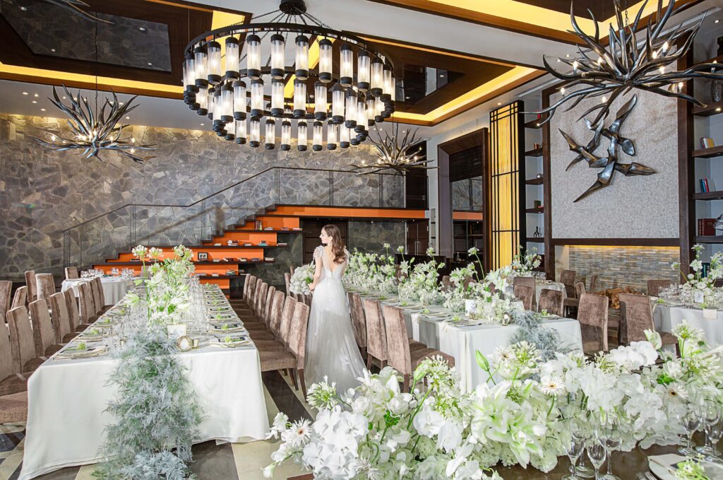 【名古屋市結婚式場ビアンカーラテラス】の象徴的な大階段と豪華なシャンデリアが目を引く披露宴会場。名古屋市にある市の中心部で、白を基調とした装花とモダンなインテリアが調和するこの空間は、名古屋市内での披露宴を夢見るお二人の理想を詳細に描写した最高の舞台です。