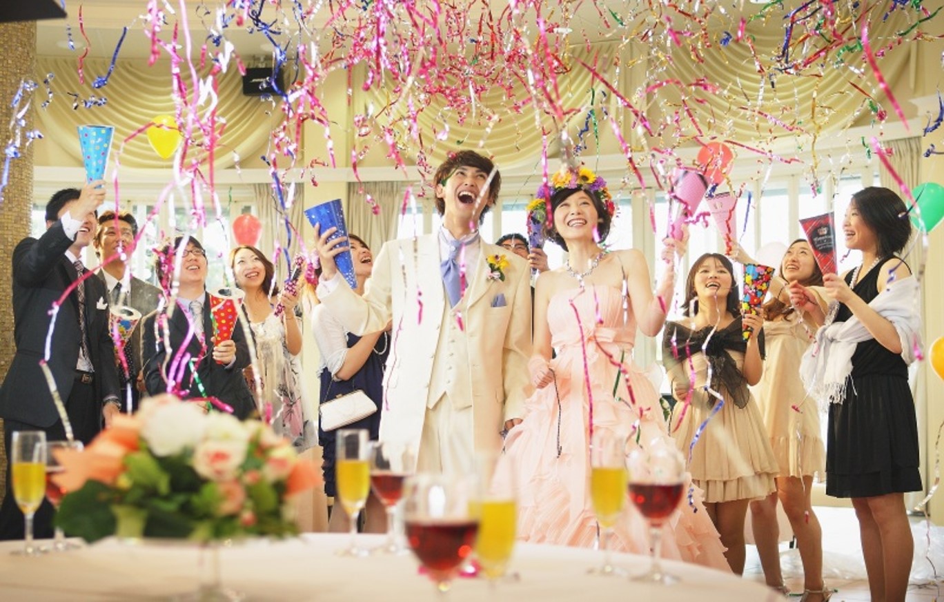 【名古屋市結婚式場ビアンカーラテラス】披露宴会場にて、ゲストからの盛大なコンフェッティで祝福される新郎新婦様。名古屋市にある市の中心部で叶える、ゲスト全員が一体となって盛り上がるアットホームな演出は、名古屋市内でも多くのカップルに選ばれる人気の高い感動的な場面を詳細に描写しています。