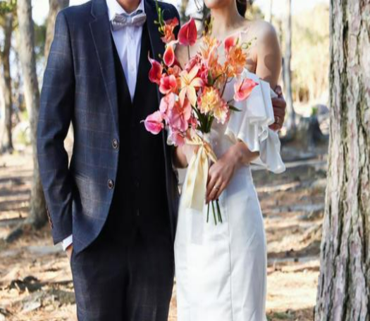 【名古屋市結婚式場ビアンカーラテラス】木々が立ち並ぶ自然豊かなロケーションで、鮮やかなオレンジ系のアンスリウムを束ねたブーケを持つ新郎新婦様。名古屋市にある市の中心部から少し離れたような開放的な森の中で撮影するウェディングフォトは、名古屋市内での結婚式をより印象的に彩る特別な一枚です。