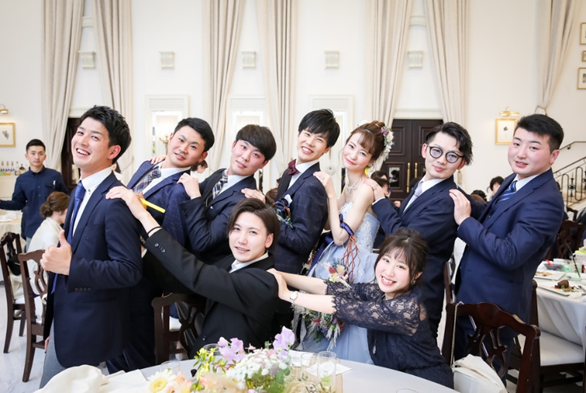 【名古屋市結婚式場ビアンカーラテラス】の白を基調とした華やかな会場にて、大切なご友人様たちと笑顔で記念撮影を楽しむ新郎新婦様。名古屋市にある市の中心部で叶える、ゲストとの距離が近いアットホームな披露宴は、名古屋市内外から集まった皆様との特別な思い出を詳細に描写した幸せ溢れるシーンです。