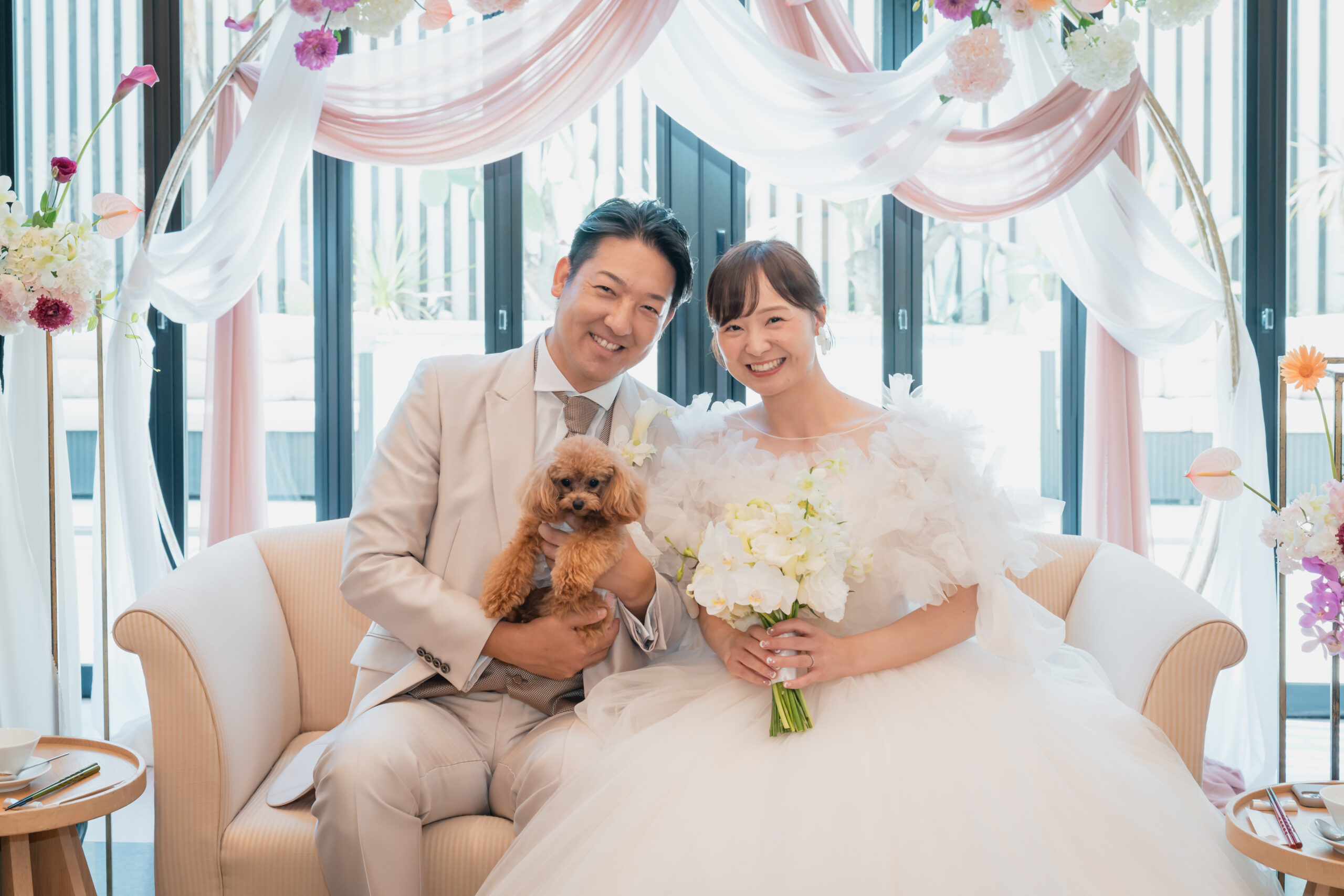 名古屋市の結婚式場ビアンカーラヒルサイドテラス。白を基調とした披露宴会場の高砂で愛犬を抱く新郎新婦。ペットと一緒に過ごせるアットホームな結婚式。