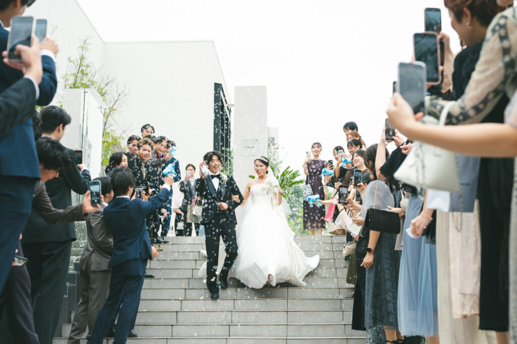 名古屋市の結婚式場ビアンカーラヒルサイドテラス。青空の下、バブルシャワーと祝福の拍手に包まれて大階段を降りる新郎新婦。ゲストと喜びを分かち合う感動の屋外挙式演出。