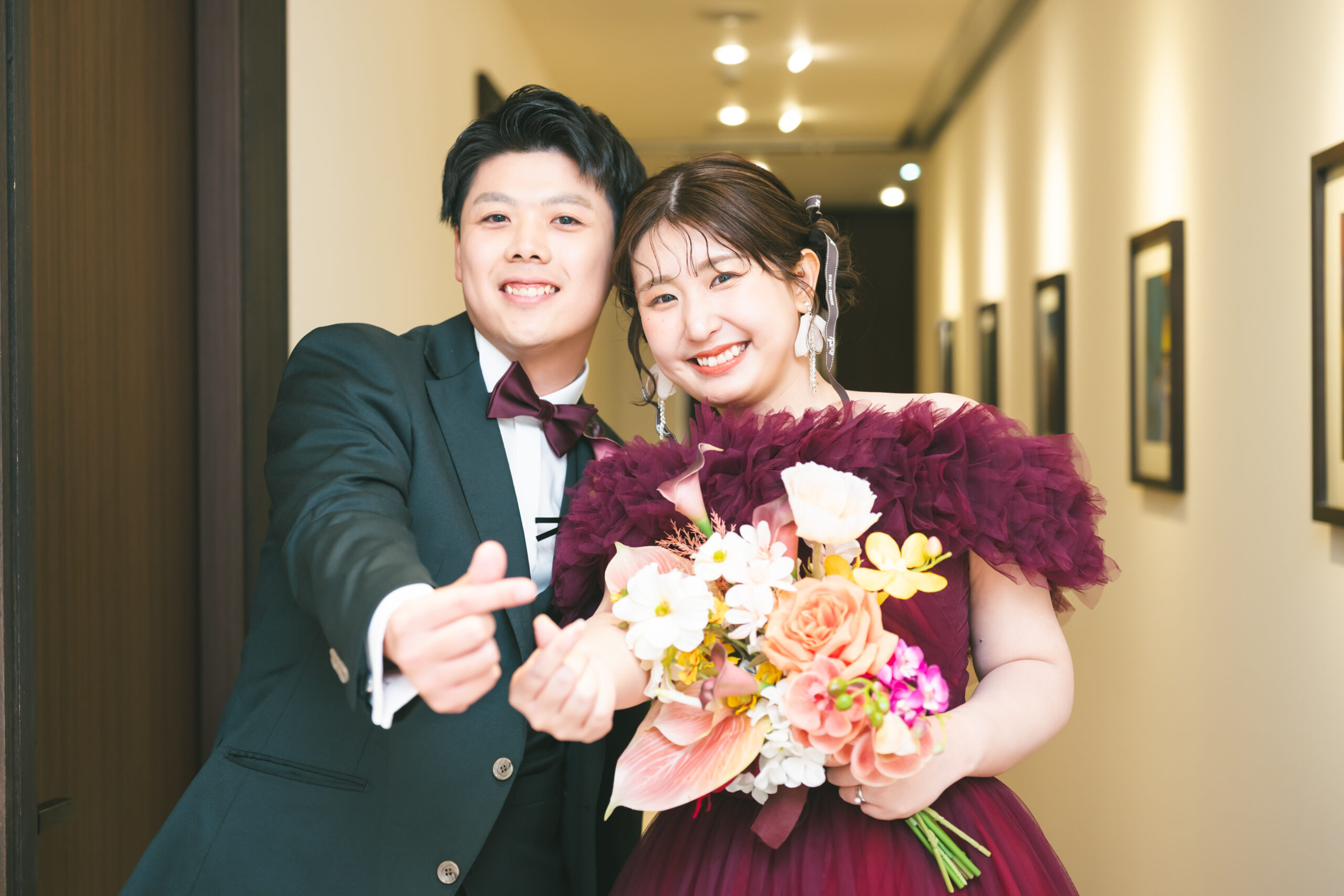 名古屋市の結婚式場ビアンカーラヒルサイドテラス。お色直し後のボルドーのドレス姿の新婦と新郎。指ハートで笑顔を見せる、幸せな披露宴のワンシーン。