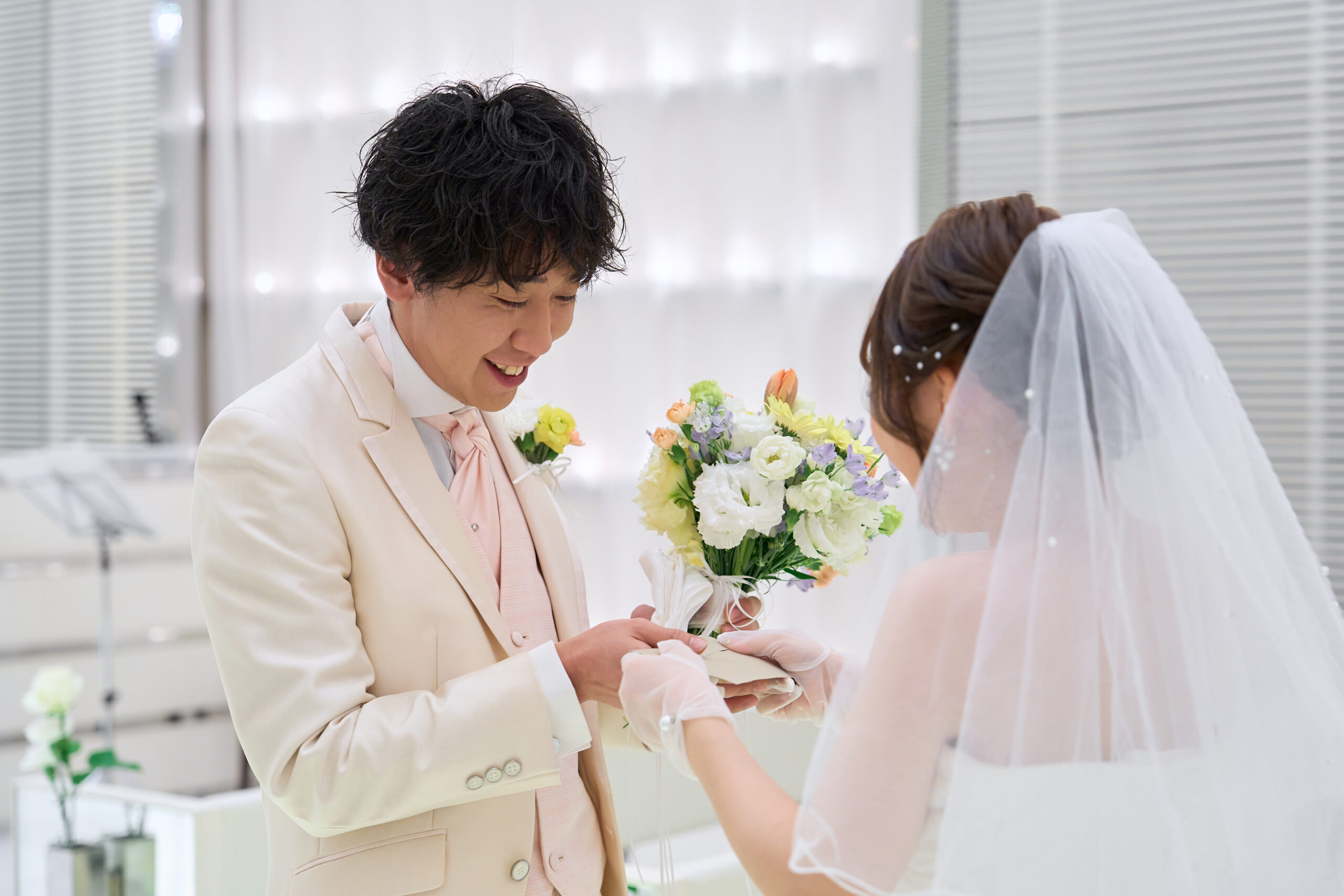 名古屋市の結婚式場ビアンカーラヒルサイドテラス。挙式で新郎から新婦へブーケを贈る感動の演出。幸せな笑顔で誓いを交わす、純白のドレス姿の新郎新婦。