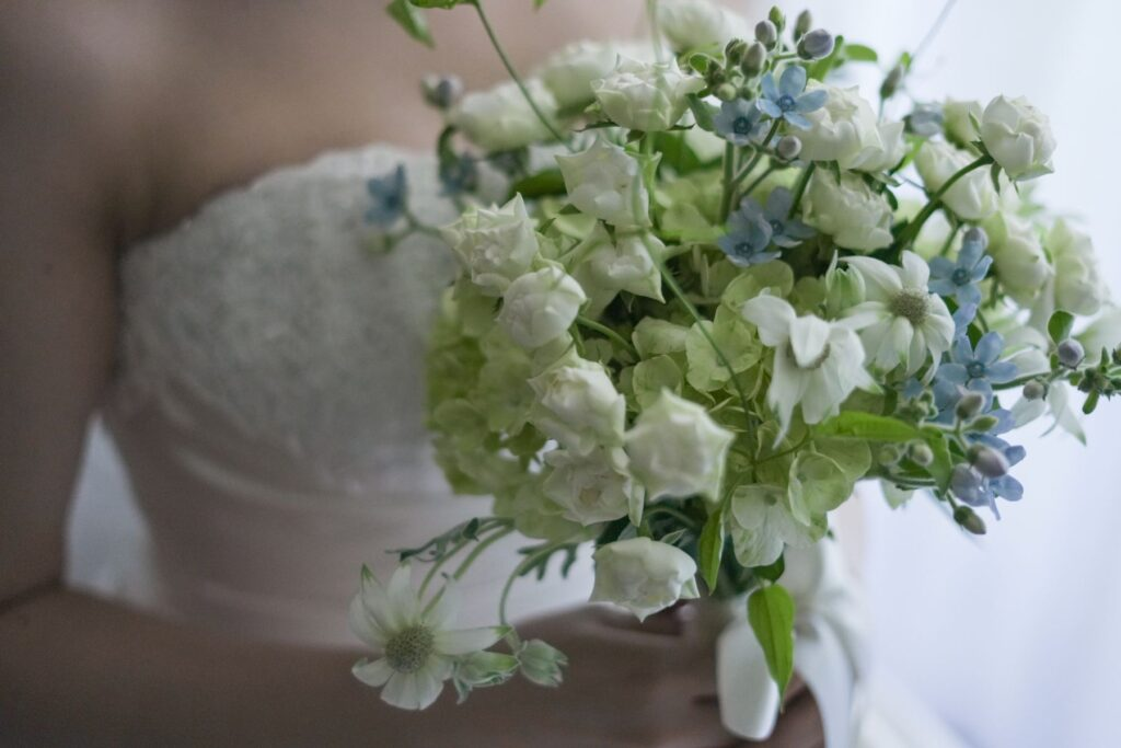 名古屋市結婚式場ビアンカーラ・ヒルサイドテラス。白のウェディングドレスを纏った新婦が持つウェディングブーケのアップ。白のミニバラや可憐な水色のブルースター、淡いグリーンのアジサイを束ねた、清楚でナチュラルなデザインのブーケ。