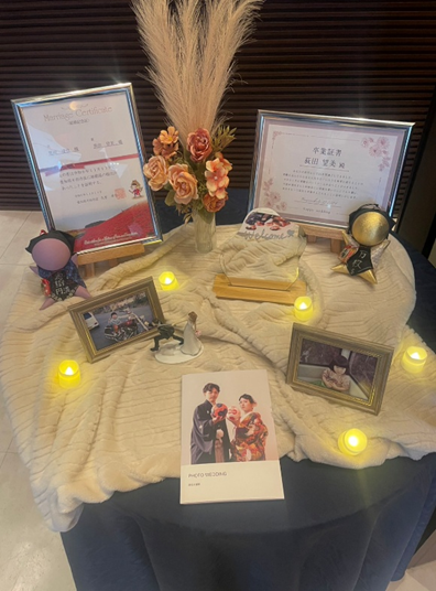 名古屋市の結婚式場ビアンカーラヒルサイドテラスの結婚式のウェルカムスペースに飾られた結婚証明書とフォトウェディングの写真、ブーケやライトを使った華やかな受付装飾。