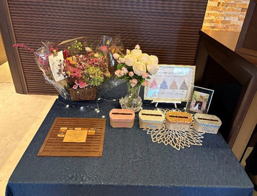 結婚式のウェルカムスペースに置かれた装飾テーブル。濃紺のクロスの上に花束や生花のアレンジ、メッセージボード、3色の投票ボックス、フォトフレームが並んでいる。