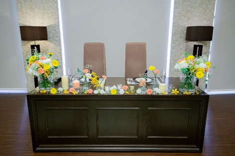 名古屋市結婚式場ビアンカーラ・ヒルサイドテラスの披露宴会場「ストーンヒルズ」のメインテーブル。イエローとオレンジの装花にキャンドルを添えた、モダンで温かみのある高砂コーディネート。