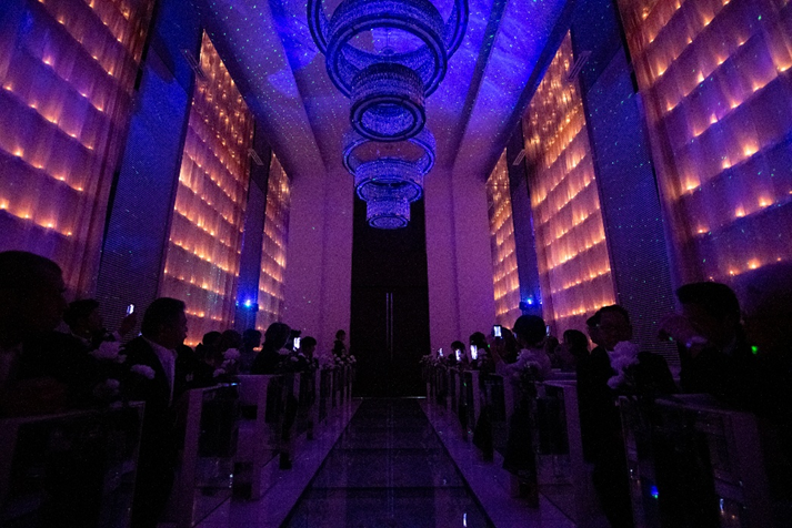 ブルーの光と星空のようなドットが天井に広がる、名古屋市結婚式場ビアンカーラ・ヒルサイドテラスのチャペル演出。壁面のキャンドルライトと青い光が織りなす、幻想的でロマンチックな挙式の雰囲気。