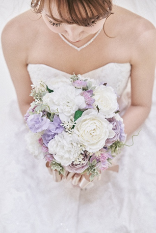 名古屋市結婚式場ビアンカーラヒルサイドテラス。白とパープルの花々を束ねた上品なウェディングブーケを手に、優しく微笑む花嫁。純白のドレスとパールのネックレスが、清楚で華やかな花嫁姿を演出。