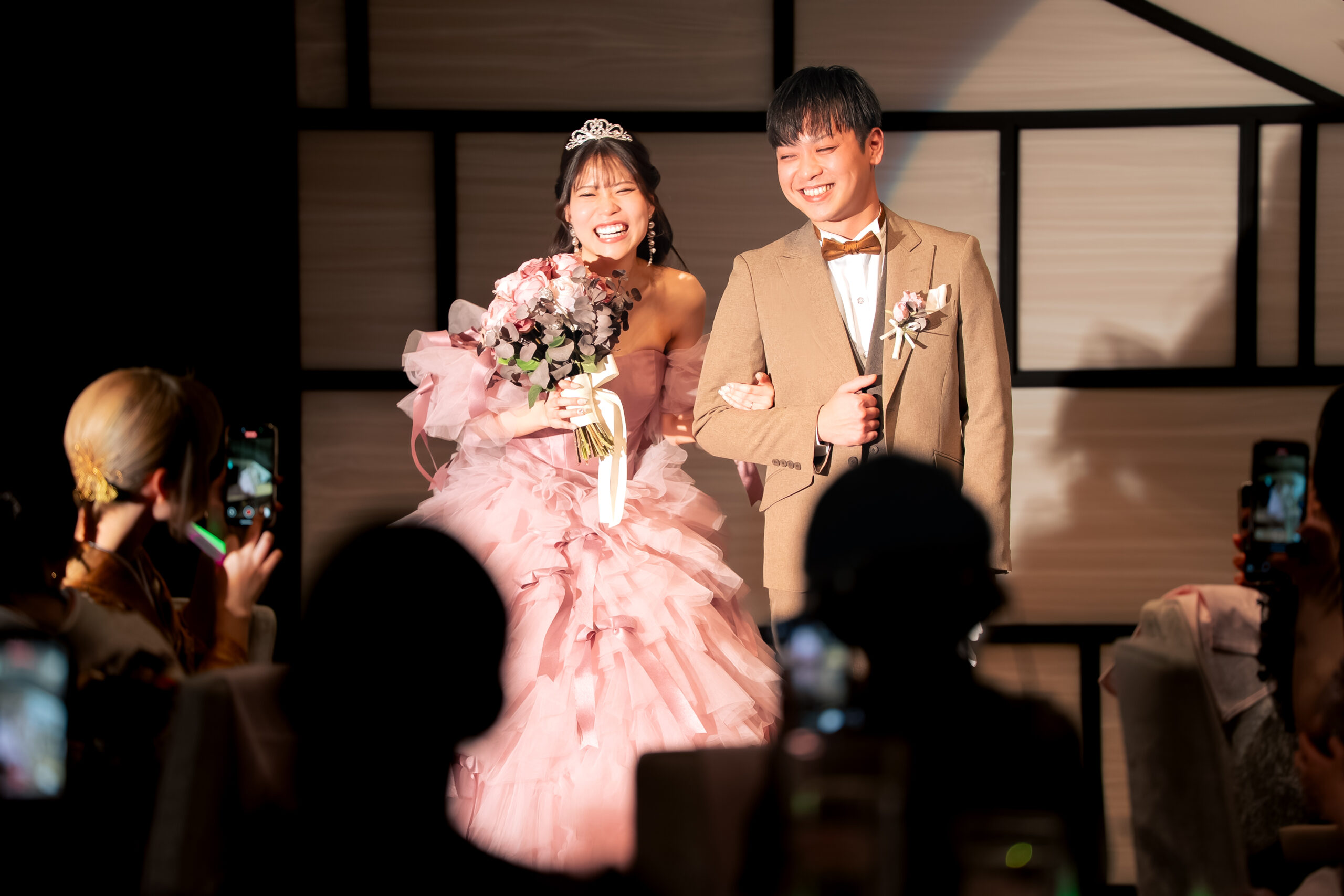 ピンクのカラードレス姿の新婦と新郎が、ゲストに祝福され笑顔で入場する様子