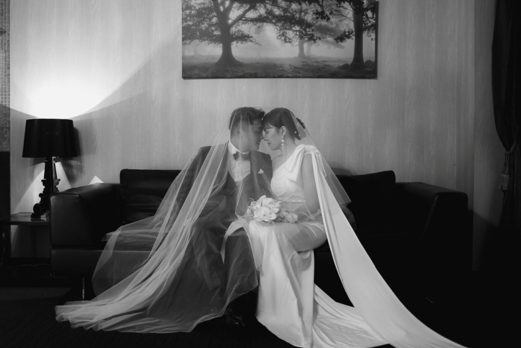 名古屋市の結婚式場ビアンカーラヒルサイドテラスのシックな館内で、ヴェールに包まれ静かに見つめ合う新郎新婦のロマンチックなモノクロウェディングフォト