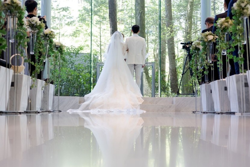 名古屋市の結婚式場ビアンカーラヒルサイドテラスのチャペル。全面ガラス張りの祭壇から森の緑が注ぎ、大理石のバージンロードに新郎新婦の姿が美しく反射する様子。