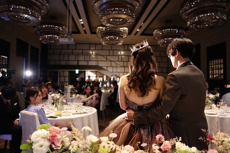 名古屋市の結婚式場ビアンカーラヒルサイドテラスの披露宴会場。豪華なシャンデリアが輝くモダンな空間で、ゲストに見守られながら新郎新婦が入場する感動のパーティーシーン。