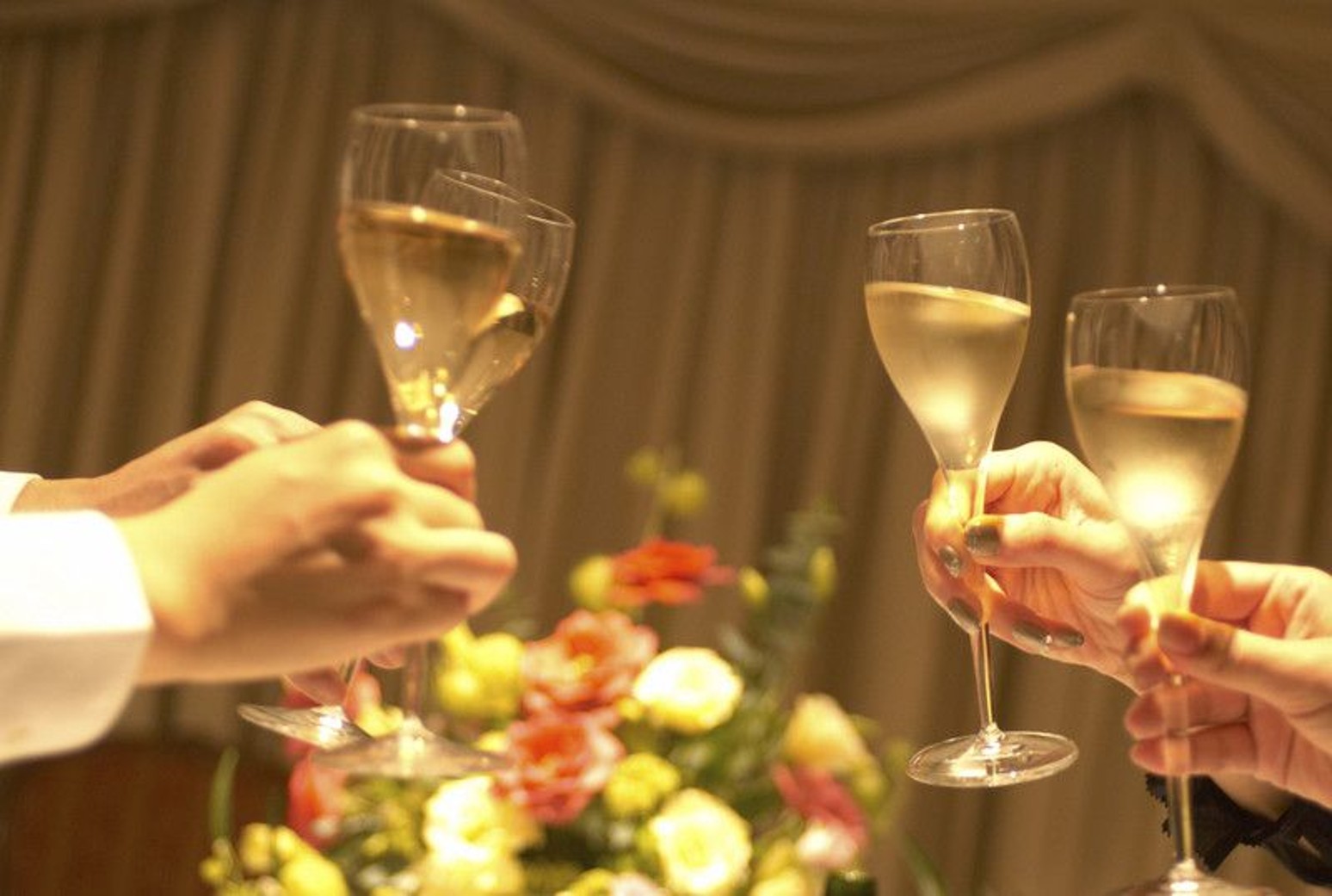 名古屋市の結婚式場ビアンカーラヒルサイドテラスの披露宴で、華やかな装花をバックにゲストとシャンパングラスで乾杯を交わす幸せなシーン。