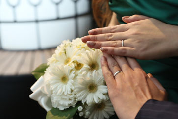 名古屋市の結婚式場ビアンカーラヒルサイドテラスで、白いガーベラのブーケに手を添え、結婚指輪を披露する新郎新婦の手元のクローズアップ。