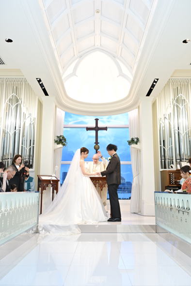 名古屋市の結婚式場ビアンカーラヒルサイドテラスの、青空が見えるチャペルで牧師から祝福を受ける新郎新婦とパイプオルガンの音色が響く挙式風景。