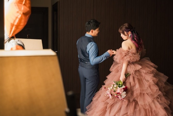 名古屋市の結婚式場ビアンカーラヒルサイドテラス。お色直しでくすみピンクのフリルドレスを纏った新婦と、ネイビーのタキシード姿の新郎が手を取り合う様子。