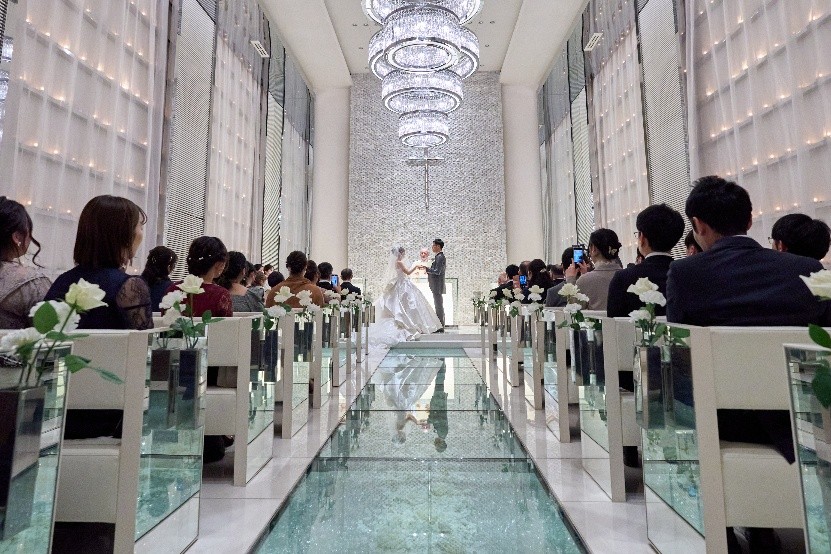 名古屋市の結婚式場ビアンカーラヒルサイドテラスのガラスのバージンロードチャペルで、700個のキャンドルの光に包まれながら挙式を行う新郎新婦とゲスト。