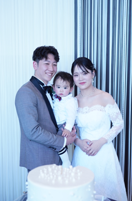 名古屋市の結婚式場ビアンカーラヒルサイドテラスで叶えるファミリー婚。ウェディングケーキを前に、お子様を抱っこして笑顔を見せる新郎新婦の幸せな一枚。